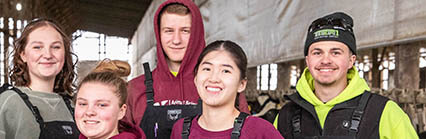 Five people in work overalls standing inside a barn-like structure