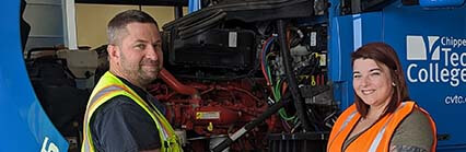 Two people in safety vests stand by a large vehicle with its engine exposed at Chippewa Valley Technical College.