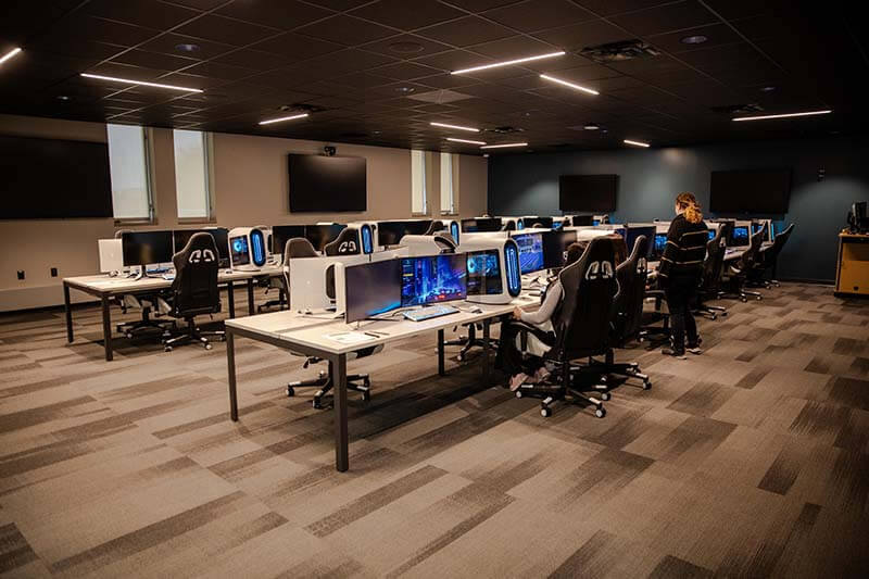 A wide-angled view of a computer classroom where a few students are seated at some of the workstations