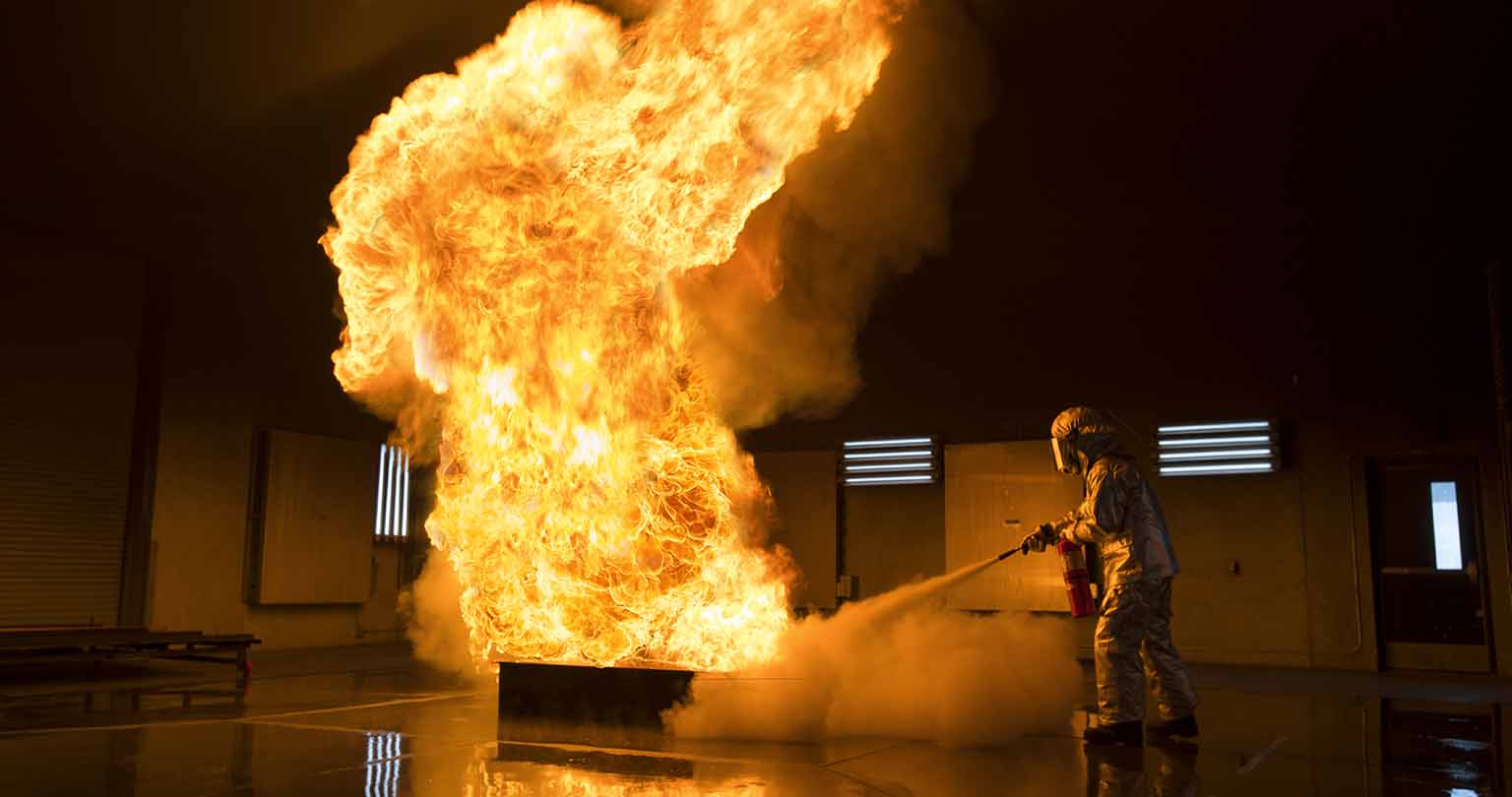 A student in fire fighting gear putting out a fire large in the Fire Safety Center.