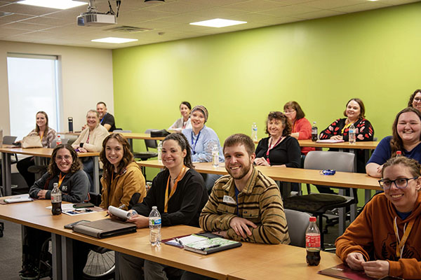 A classroom full of adult students smiling and with conference materials at the tables