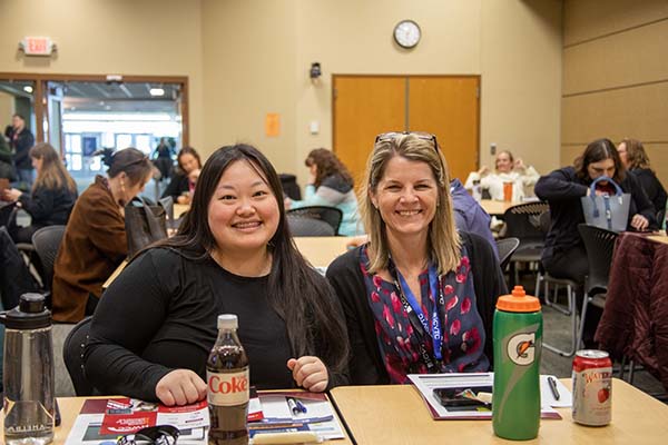 Two women sitting at a table in a conference room smiling