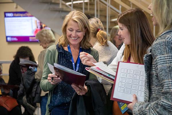 Two women in a conference room standing and talking with each other while looking over their conference materials