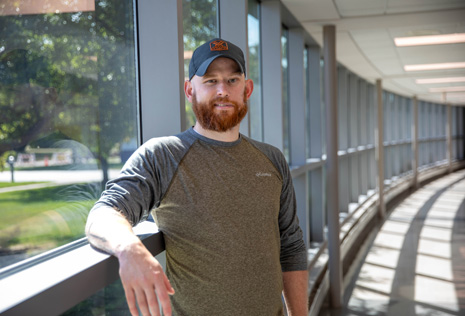 man with baseball cap standing in a hallway with windows