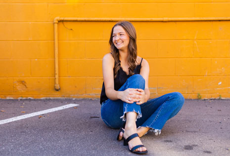 Girl with long brown hair sitting on the ground in front of yellow wall