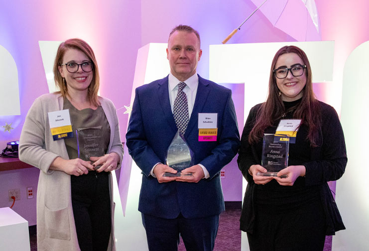 two females, one male with awards at a gala event